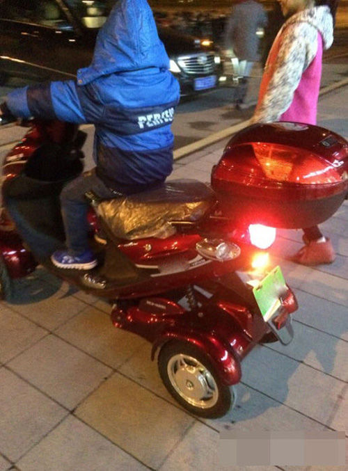一个身穿蓝色棉衣的小男孩正骑着电动车，而他身边站着一个身穿粉色上衣的小女孩；而另一张照片则可以清楚地看到小男孩拿出一沓红包放在营业员面前。
